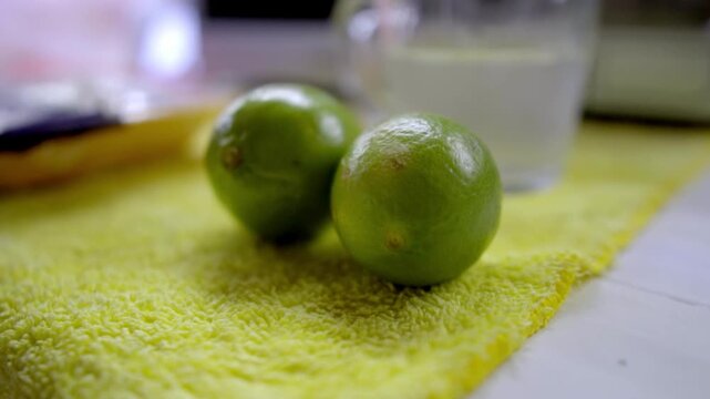 Close view of fresh limes placed on yellow cloth, citrus fruits ready for cooking or seasoning, simple kitchen setup with soft background and natural light