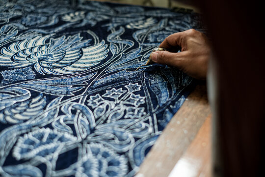 Detail shot of a copper canting tool tracing intricate floral patterns with melted wax on fabric. Showcasing the authentic precision of Indonesian batik tulis craftsmanship.