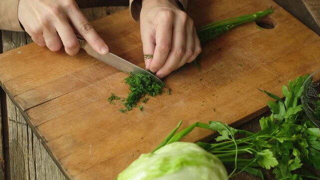 Female hands cutting dill on wooden chopping board in kitchen
