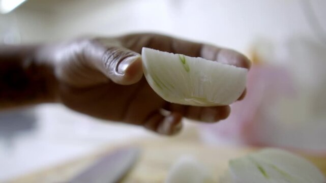Close view of hand holding sliced onion piece, fresh vegetable segment ready for cutting or mixing, simple food preparation step in kitchen with soft focus background
