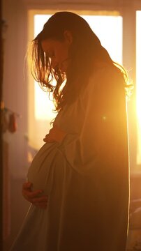 Pregnant woman gently caressing her baby bump, illuminated by the golden morning sun streaming through a window. A beautiful silhouette captures the intimate bond between mother and child
