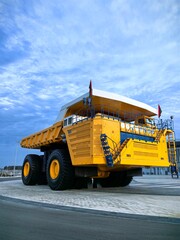 Low angle view of a giant yellow mining dump truck with massive tires, blue metal stairs and safety railings against dramatic cloudy blue sky. Heavy industrial mining vehicle concept. © Алина Неборская