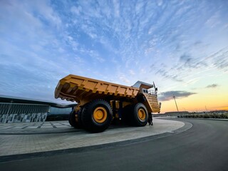 Low angle view of a giant yellow mining dump truck with massive tires, blue metal stairs and safety railings against dramatic cloudy blue sky. Heavy industrial mining vehicle concept. © Алина Неборская