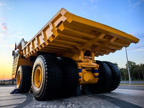 Low angle view of a giant yellow mining dump truck with massive tires, blue metal stairs and safety railings against dramatic cloudy blue sky. Heavy industrial mining vehicle concept.