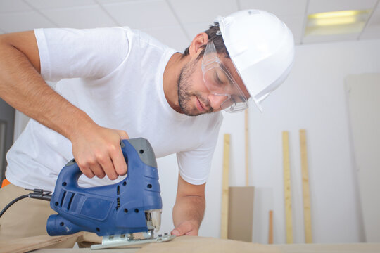 man cutting wood block with fretsaw at the workshop