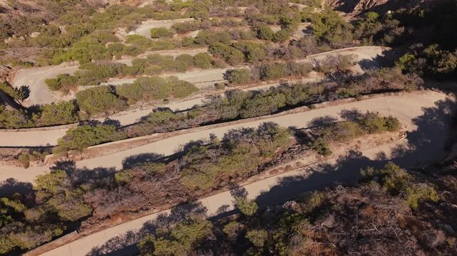 A sweeping panoramic drone view starting on the intense zigzag switchbacks climbing Mesa Vouno mountain, pulling back to reveal the full expanse of Kamari Beach and the dark volcanic coastline below.