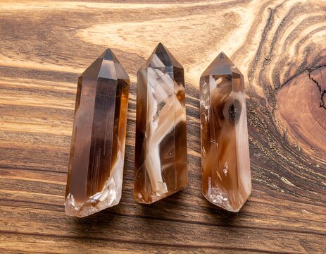 Three columnar crystals, with brown and white banding, stand on a rustic, wood-grain surface. Light reflects off facets