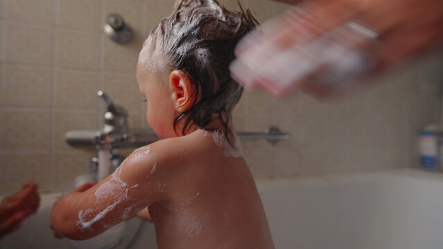 Mother styling toddler&rsquo;s wet hair into playful punk shape with shampoo foam during bath time, happy child smiling, fun and intimate family bonding moment at home