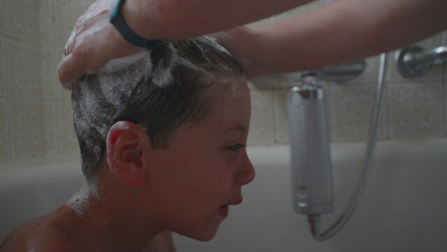 Mother washing child&rsquo;s hair with shampoo, creating foam and lather during bath time, joyful and intimate family bonding moment in cozy home bathroom
