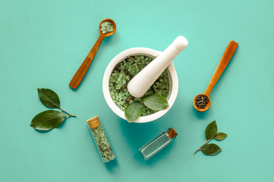 Homemade organic cosmetics products - tea tree essential oil and sea salt in mortar and pestle with green leaves on green background, top view.