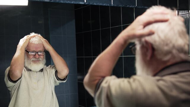 Old man stands in front of mirror. He ruffle turn his hairstyle into chaos