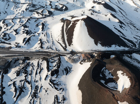 Aerial view of the snow-covered volcanic craters and dark lava fields on the southern side of Mount Etna in Nicolosi, Sicilia, Italy.