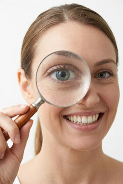 Woman holding magnifying glass in front of eye, enlarging eye. Searching for something, solving mystery and case.