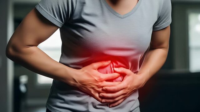 Woman suffering from acute abdominal pain holding her stomach area with both hands while feeling extreme distress and discomfort due to a sudden internal health medical issue