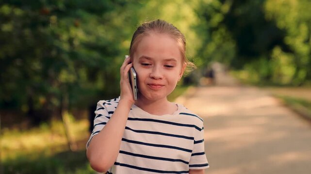Little girl talking on phone in park, Smiling child on smartphone outdoors, Young girl making phone call in nature, Cute kid chatting on mobile in park, Happy girl with cellphone on walking path