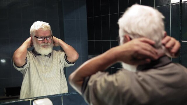 Elderly man stands in front of mirror. He ruffle turn his hairstyle into chaos