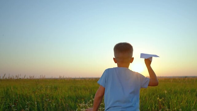Boy throws paper airplane in field at sunset. Child plays with paper plane outdoors. Kid launches aircraft in meadow. Boy throwing paper glider. Child plays with airplane at golden hour.