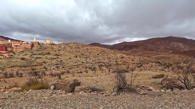 Scenic drive passing a traditional berber village with a minaret in the arid atlas mountains of morocco under a cloudy sky