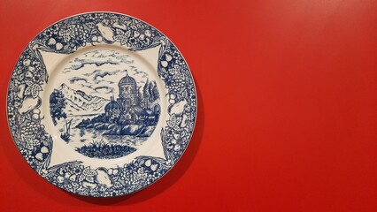 a classic plate with a motif depicting natural scenery and castle buildings. Placed on a red table © Rudy