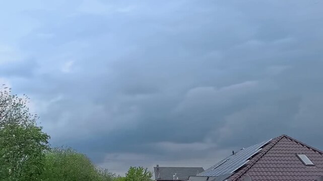 Dramatischer Zeitraffer: Aufziehendes Unwetter und dunkle Gewitterwolken &uuml;ber Wohnhaus mit Solaranlage