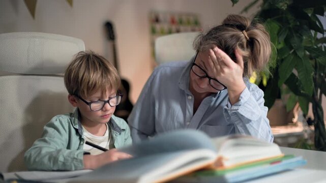 Mother helping her son with homework and check it, both are really tired of it