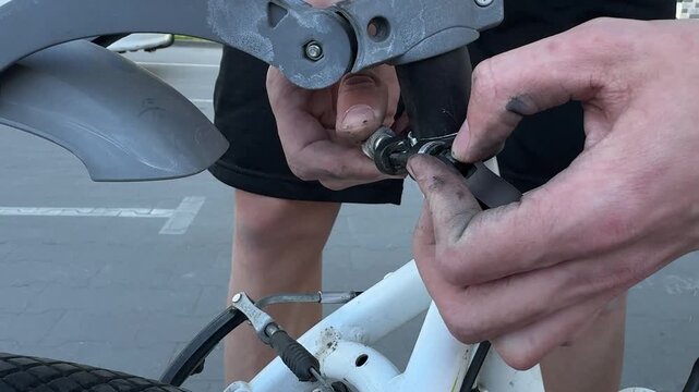 Hands adjusting bicycle seat post clamp on a white bike outdoors. Bicycle repair, bike maintenance, cycling service, mechanical work.