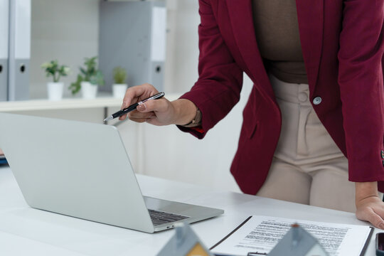Standing Asian Female Real Estate Agent Pointing at Laptop Screen in Office