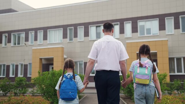 child kid schoolgirls go to school parent, father leads child kid baby with backpacks school lesson, child education school, little girl dad walking hand hand school yard, view from back, man lead