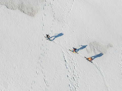Aerial view of three skiers trekking across a pristine snow-covered slope on Mount Etna, leaving tracks and long shadows on the white surface Nicolosi, Sicilia, Italy.