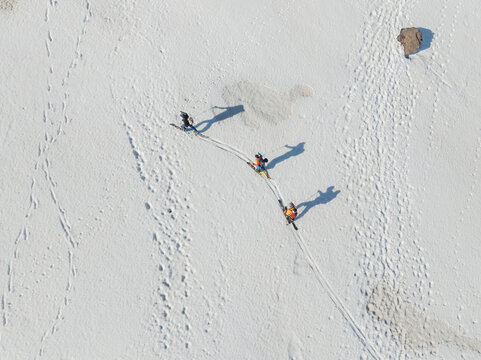 Aerial view of three skiers trekking across the snowy slopes of Versante sud dell' Etna with long shadows and tracks on the white surface Nicolosi, Sicilia, Italy.
