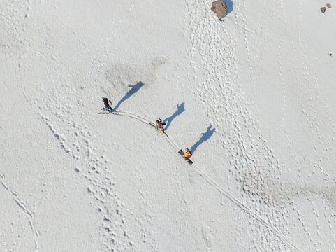 Aerial view of three skiers descending the snow-covered south slope of Mount Etna with long shadows and tracks in Nicolosi, Sicilia, Italy.