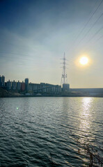 Fototapeta premium A serene urban scene features a sunset reflecting on calm water, with buildings and power lines nearby