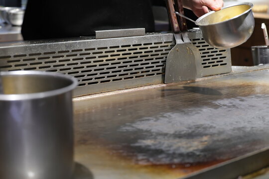 A professional chef prepares the teppanyaki grill with sauce.