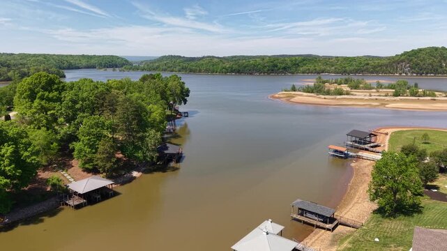 Aerial drone footage over the Hiwassee River near Georgetown Tennessee showing boat docks boathouses and riverfront residential properties surrounded by lush green forest with sandy shoreline