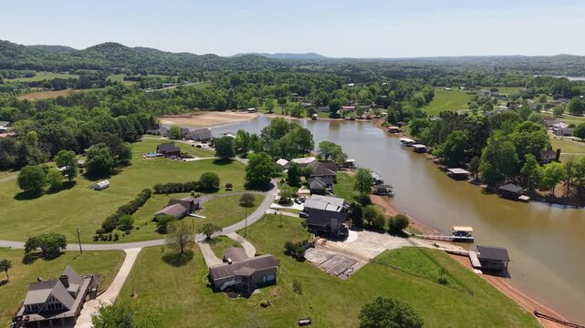 Low altitude drone flyover of the Georgetown Tennessee rural community featuring homes green lawns vehicles and a dirt road with the Hiwassee River curving through the right and distant wooded ridges