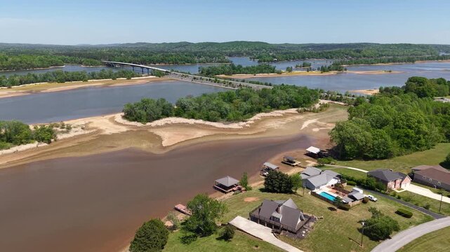 Aerial drone footage looking across the Hiwassee River near Georgetown Tennessee with exposed sandy banks riverfront homes and properties on the right and forested hills visible in the far background