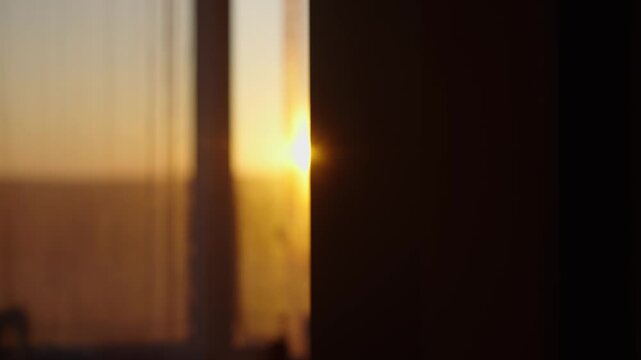 Bright morning sunbeam peaking through a window with a sheer curtain, illuminating a dim room with its warm, golden rays and creating a beautiful, atmospheric lens flare effect