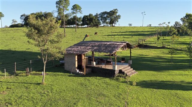 A rustic quincho with a thatched roof sits on a sprawling green farm. Suitable for rural tourism promotions or agritourism features.