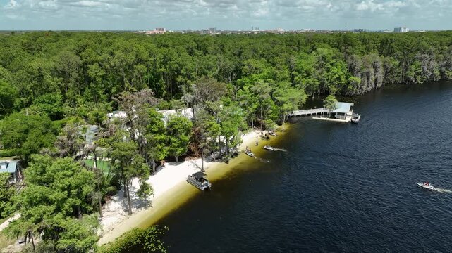 Sunny drone shot of Paradise Cove on Lake Bryan in Orlando, Florida &mdash; boats gliding across calm water, lush green forests, and a charming waterfront getaway nestled in the trees.