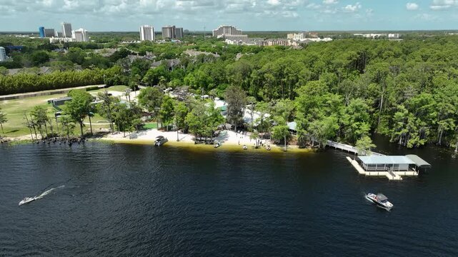 Aerial drone view of Paradise Cove in Orlando, Florida, featuring a tropical lakeside retreat, sandy shoreline, lush palm trees, and boats cruising across the blue waters of Lake Bryan.