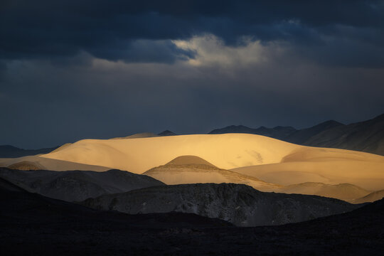 Golden light on sand dunes in Puna de Atacama Argentina during storm. Dramatic spotlight on desert mountain landscape. Ideal for fine art prints.