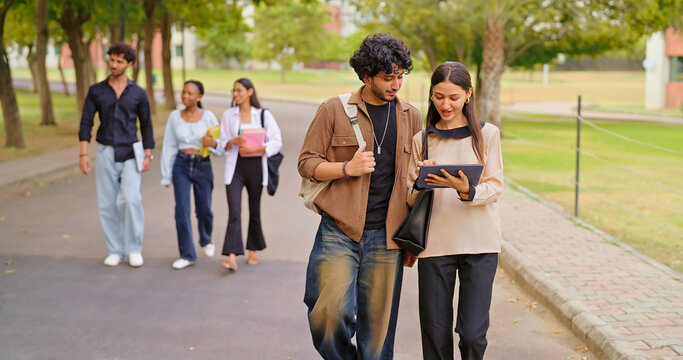Indian young adult gen z busy boy girl use tab look screen talk share new online e learning study plan place. pupil female male man group speak funny gossip enjoy break day have fun joy park