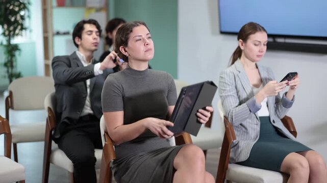 Focused group of students sitting on chairs and listening lecture, taking photo or QR with mobil or tablet in light lecture hall