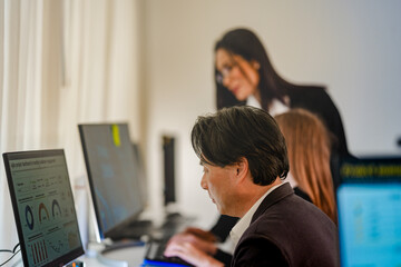 Fototapeta premium Diverse corporate engineers collaborating on privacy preserving AI. Asian female machine learning specialist helping coworker with secure coding behind blurred foreground monitor.