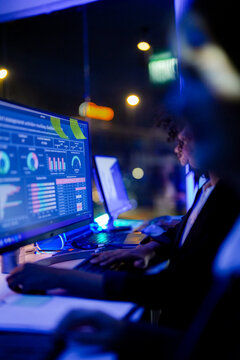 IT specialists and data analysts monitoring real-time cybersecurity dashboards and network metrics in a high-tech operations center at night.