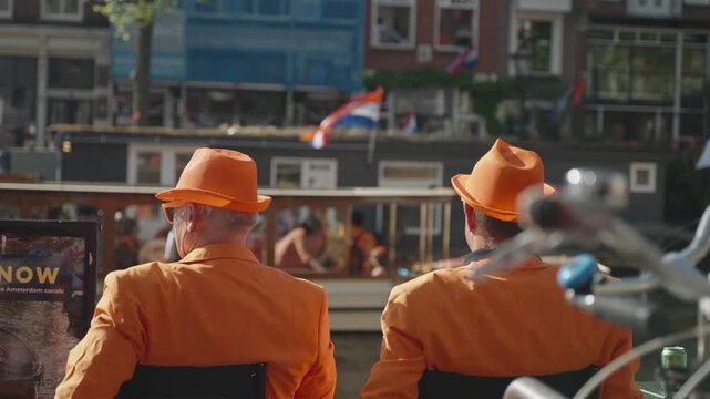 King's Day in Amsterdam. Two men near Channel in Orange Suites are Waving to Passing by Boats on Sunny Dutch Holiday.