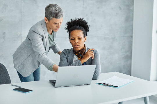 Portrait of two of young businesswomen multiethnic working with laptop on desk and talking in a start up office