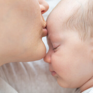 Mother kissing forehead of sleeping newborn baby