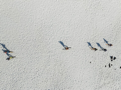 Aerial view of skiers walking across the snowy south slope of Mount Etna with long shadows on the textured white surface Nicolosi, Sicilia, Italy.