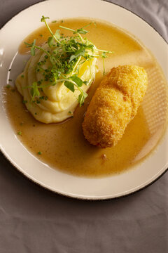 Golden croquette with silky veloute sauce, whipped potato quenelle topped with pea shoots, gourmet plating under warm light, server presenting plate in intimate bistro,